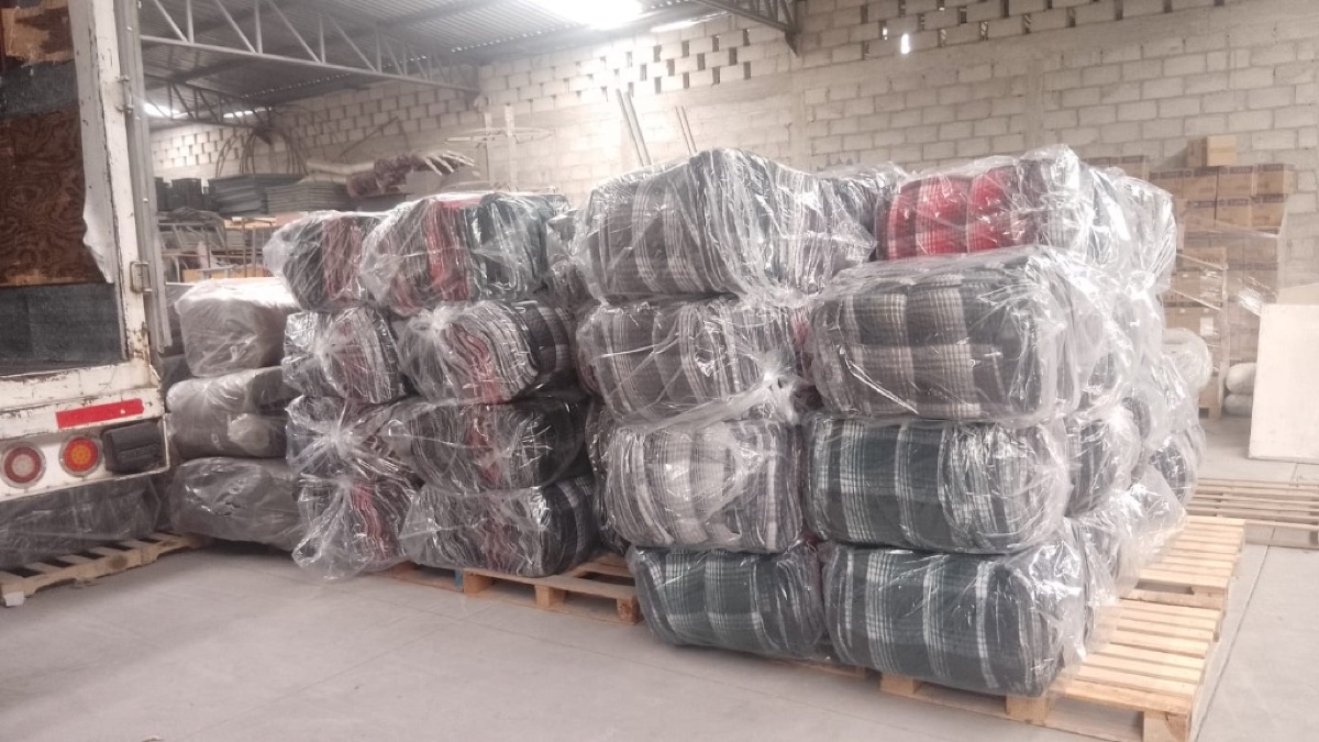 Tarimas con paquetes y pacas de cobijas en bodega listas para embarque.